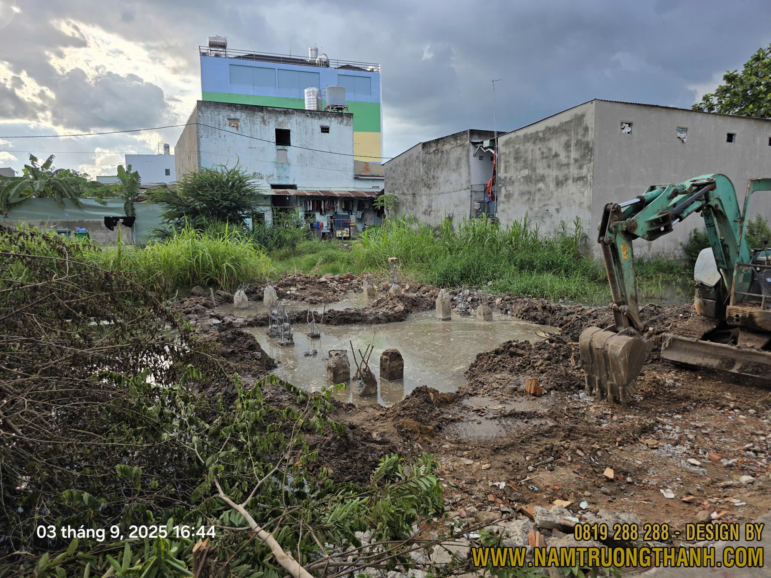 Công trình đang ép cọc móng, khu đất có nước đọng, nhiều đầu cọc lộ ra, máy xúc thi công bên phải.