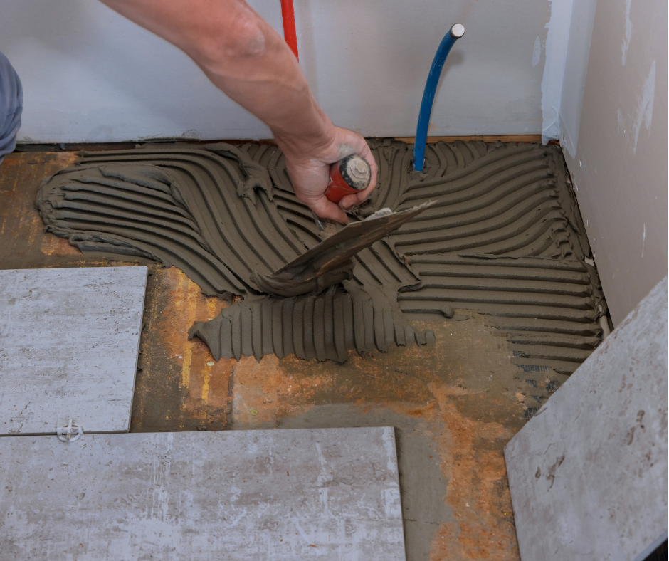 Thợ đang dùng bay răng cưa trải keo lên nền để lát gạch.