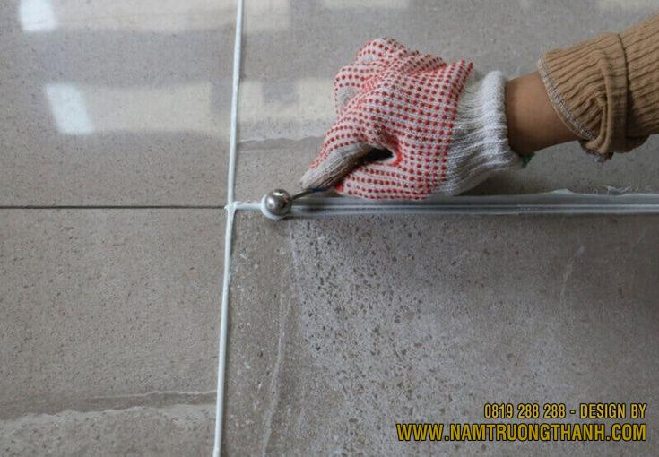 Thợ thi công đeo găng tay dùng quả cầu bi sắt miết dọc theo đường keo vừa bắn.